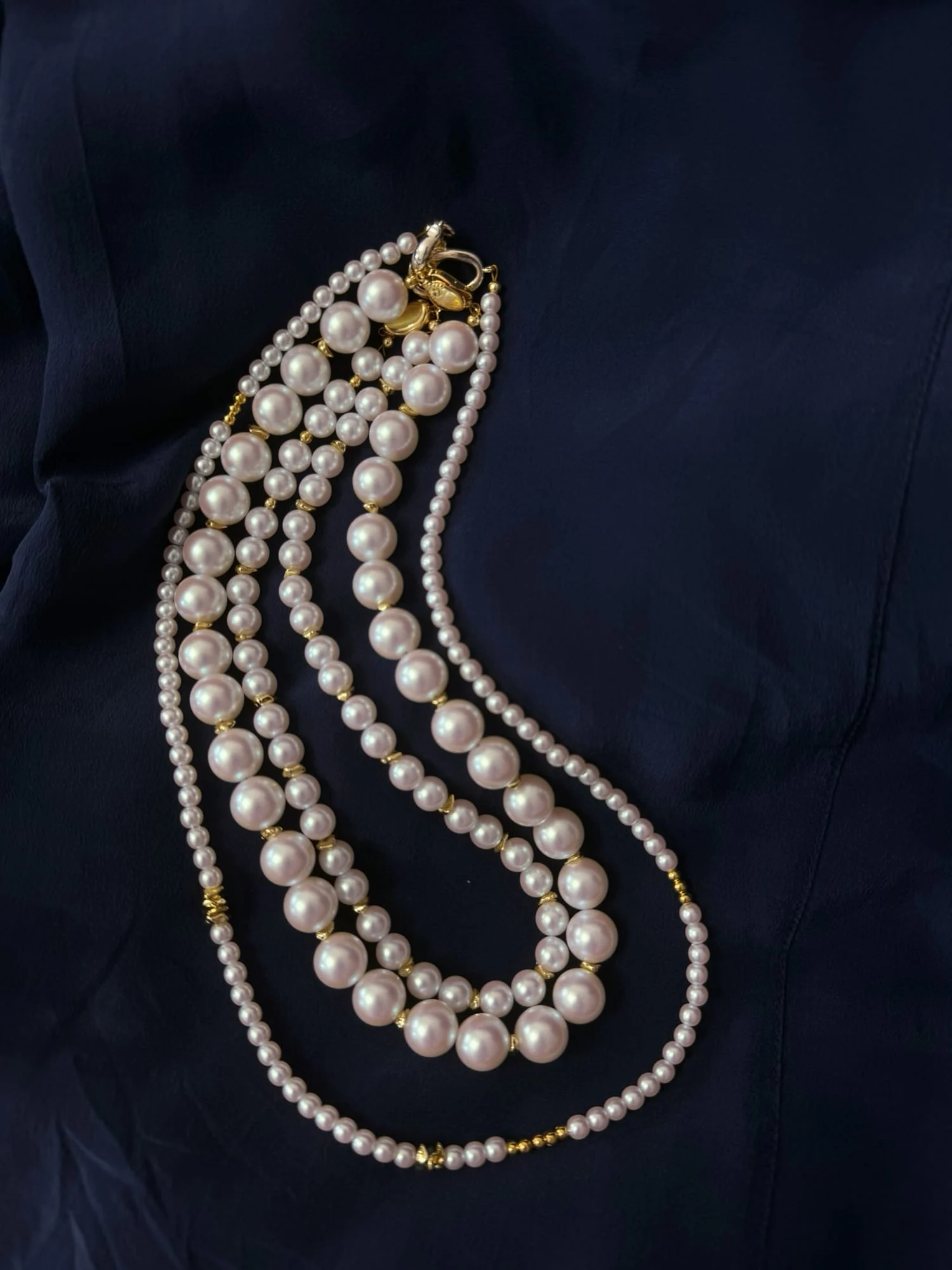 Laid on navy fabric, the white-bead necklaces stacked together: the double-strand graduated necklace, the single-strand bead necklace and the fine bead long necklace, clasps gathered at the top.