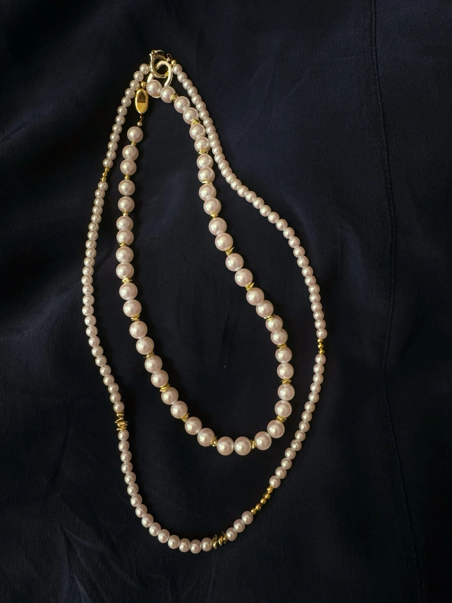 Two white-bead necklaces laid on navy fabric: the single-strand bead necklace and the fine bead long necklace, clasps at the top.