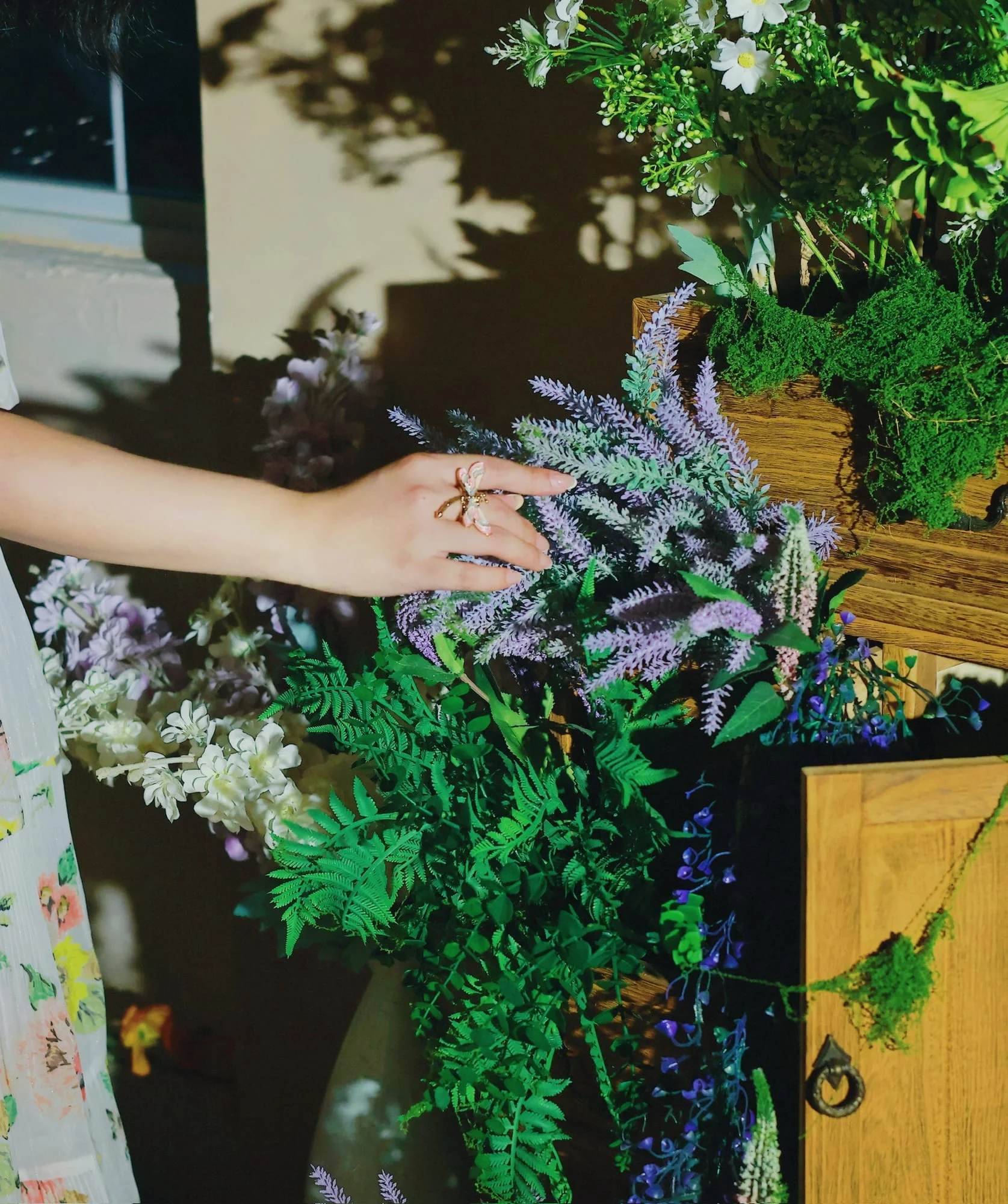 Hand wearing the pink and white enamel butterfly ring, reaching into lavender-coloured artificial flowers, white floral dress.