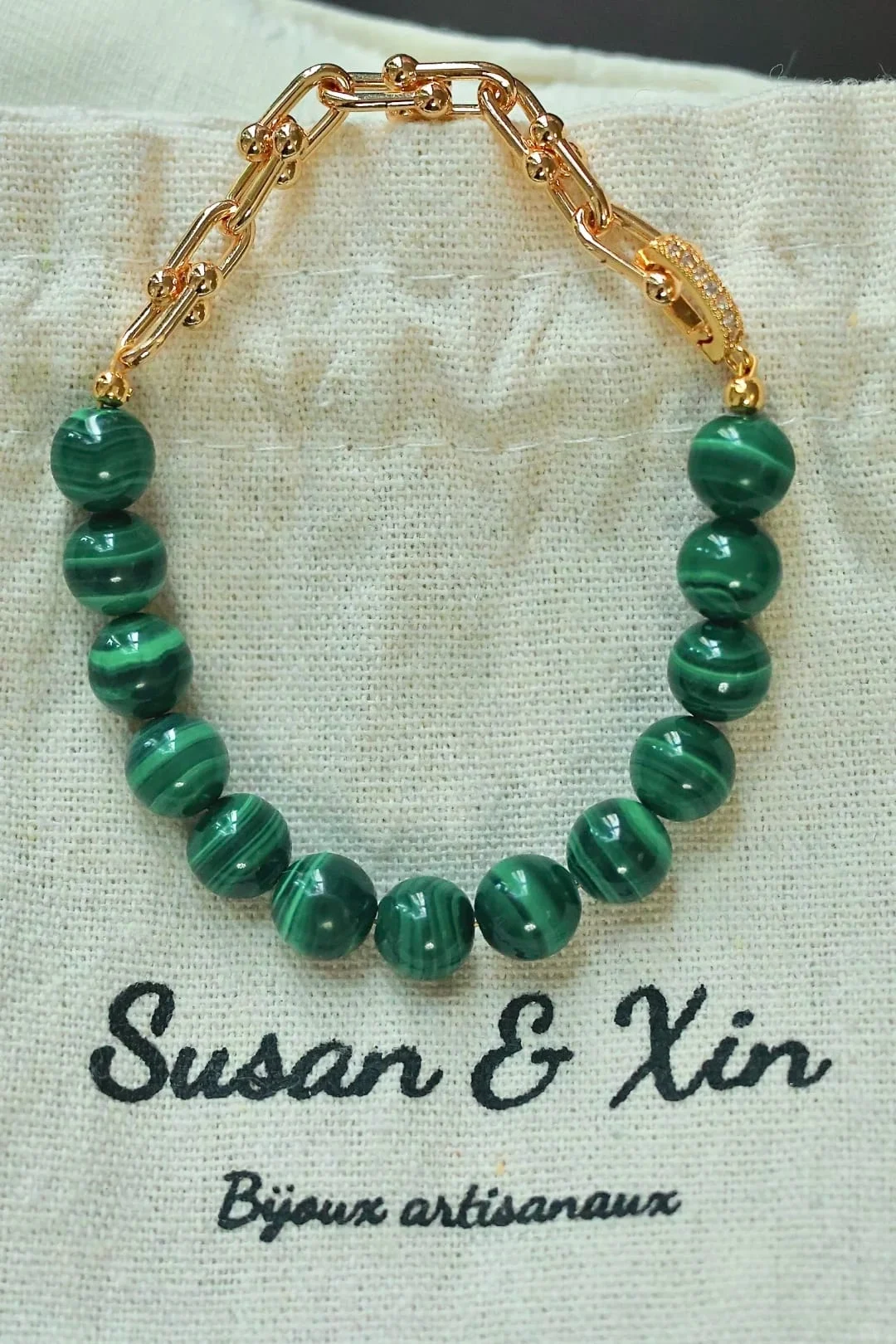 Bracelet with half a ring of large banded malachite beads and a chunky gold-toned U-link chain, its clasp set with tiny clear accents, on a Susan&Xin fabric pouch.